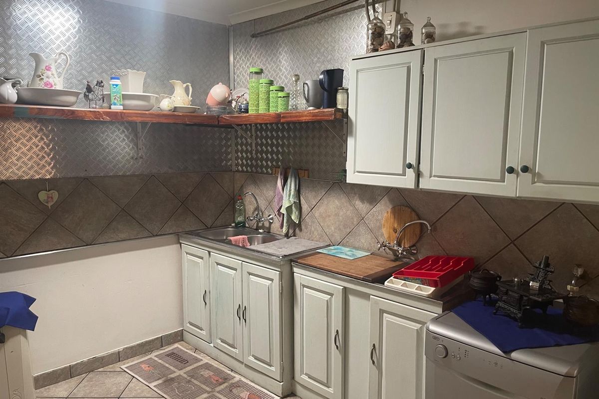 A functional kitchen area featuring light-toned cabinetry, a stainless steel sink, tiled backsplash, and metal-look wall paneling.