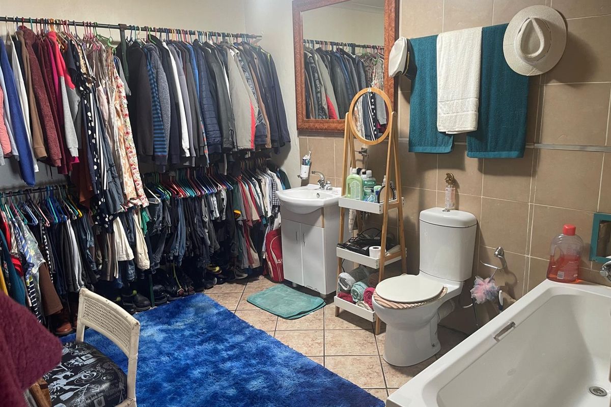 A functional bathroom featuring a bathtub, toilet, and pedestal sink with tiled walls and flooring, currently utilized for additional clothing storage.