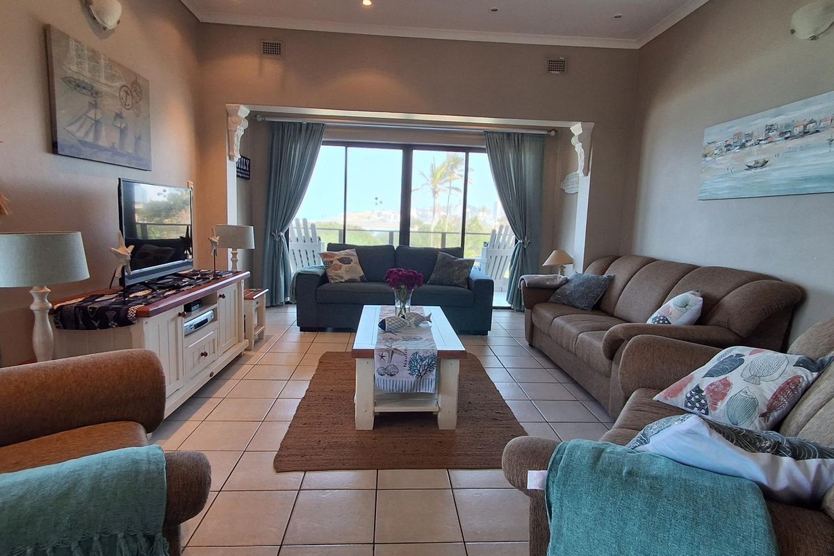 A comfortable living room featuring tiled flooring, recessed ceiling lighting, and large sliding glass doors that provide access to a balcony with scenic views.