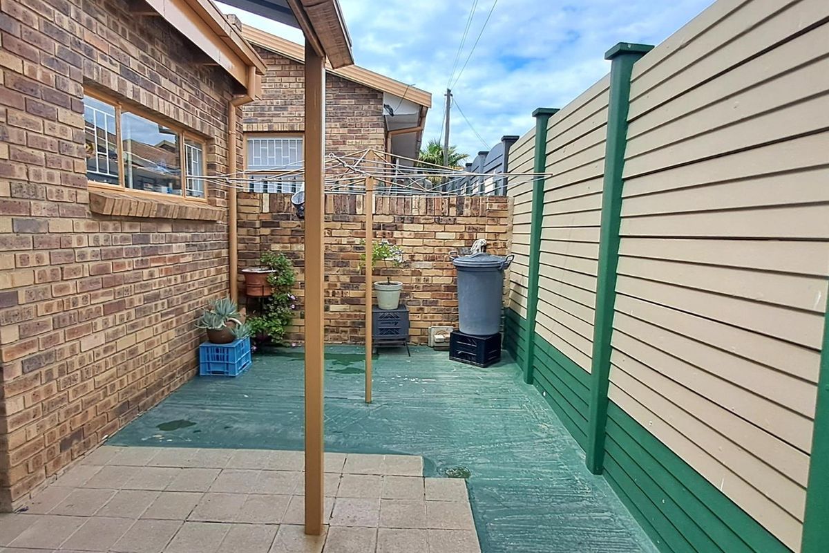 A private rear courtyard featuring a paved section, painted concrete flooring, and a perimeter timber fence with a fixed rotary clothesline.