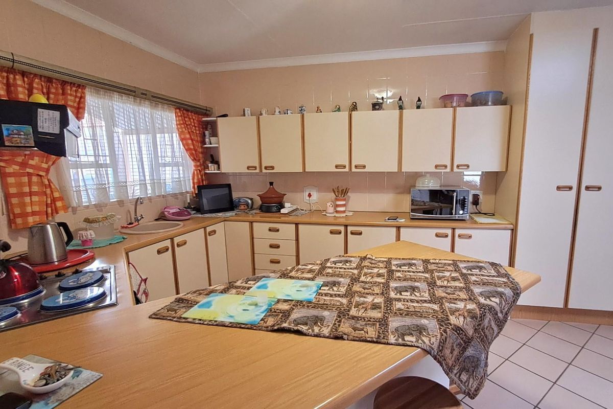 A functional kitchen featuring laminate countertops, ample built-in cabinetry, a tiled backsplash, and a breakfast nook area with tiled flooring.