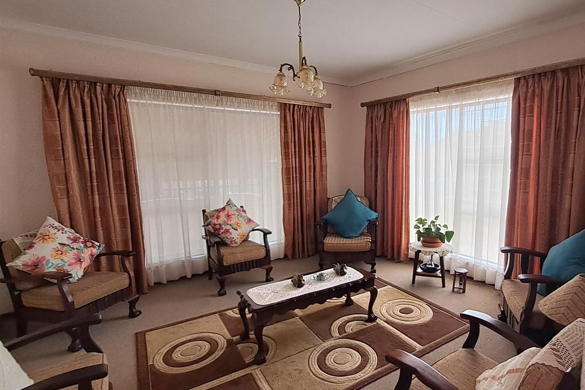 A spacious living room featuring large windows with curtain tracks, neutral carpeting, and a central ceiling light fixture.