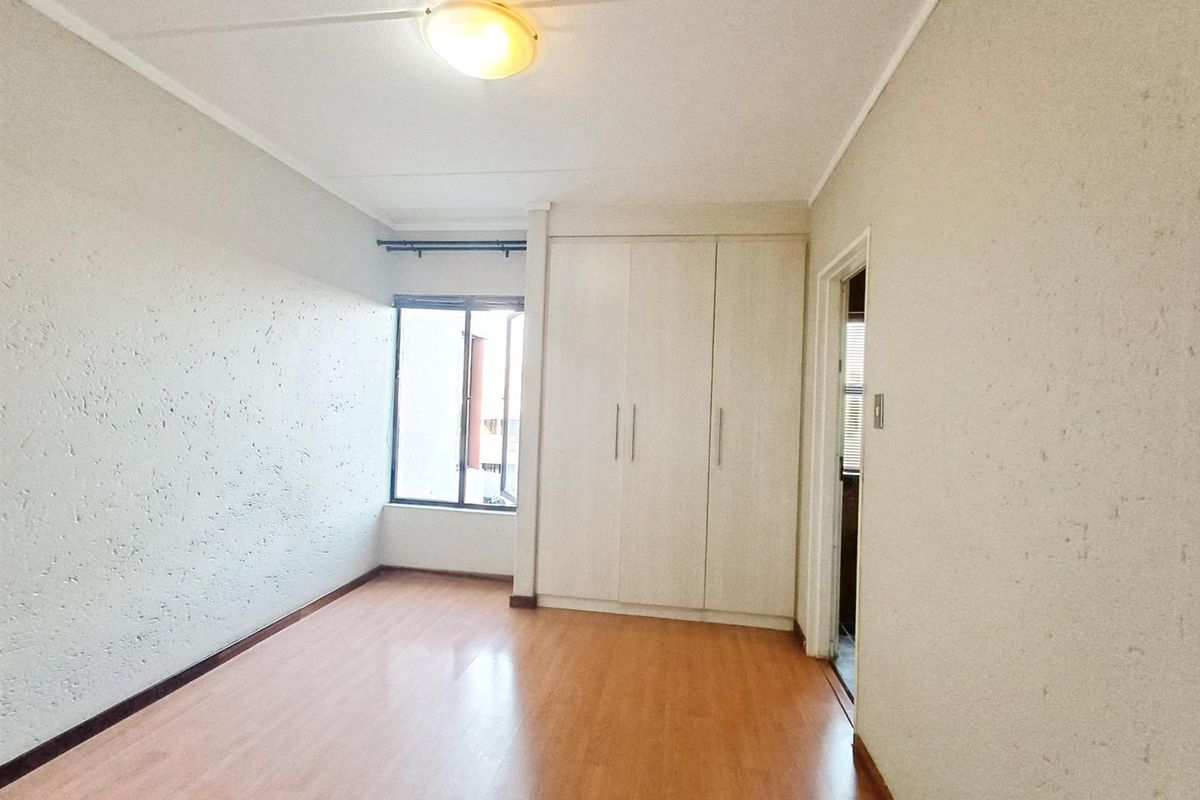 A bright, empty bedroom featuring laminate flooring, built-in cupboards, and a window providing natural light.