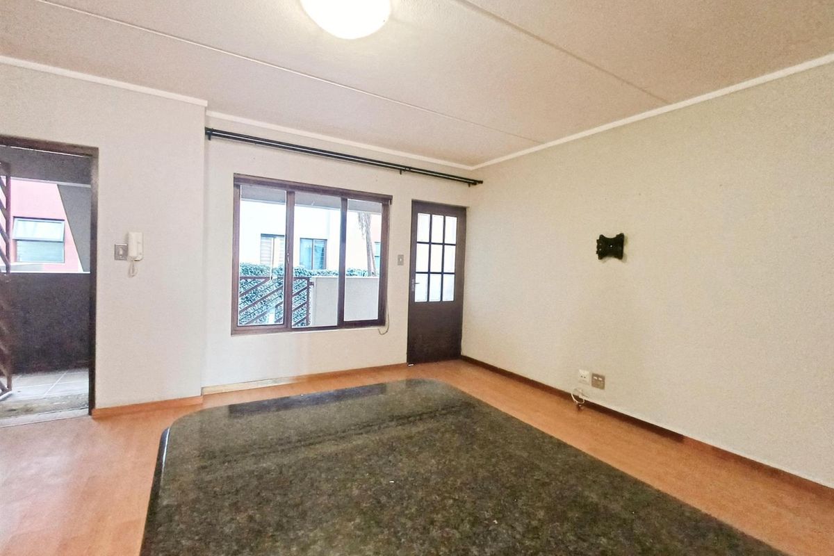An empty living room featuring laminate flooring, a large window, and a glass-paneled door leading to an exterior walkway.