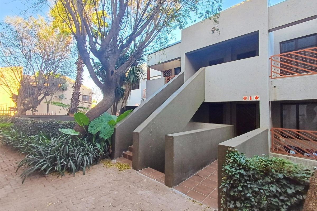 Exterior view of an apartment complex featuring a concrete staircase, paved walkway, and established garden landscaping.