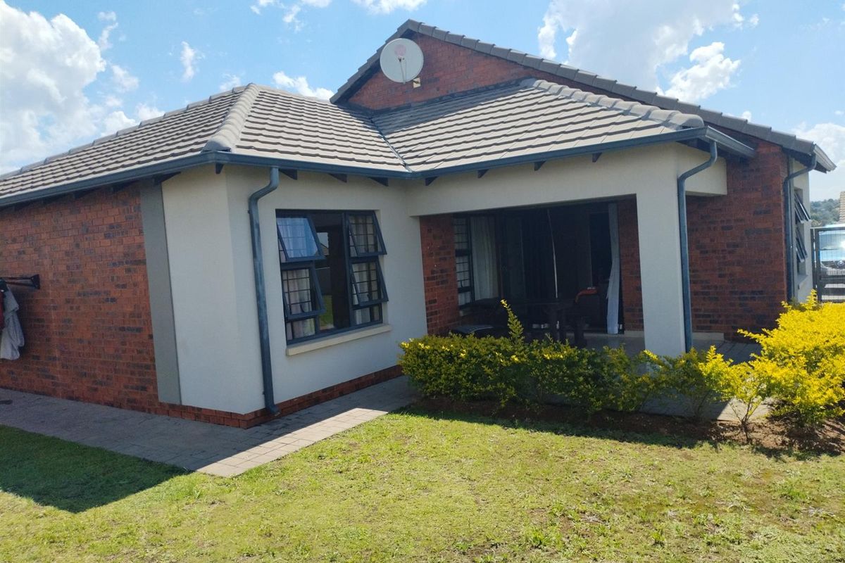 Rear view of a brick house featuring a covered patio, tiled roof, and a well-maintained garden area.