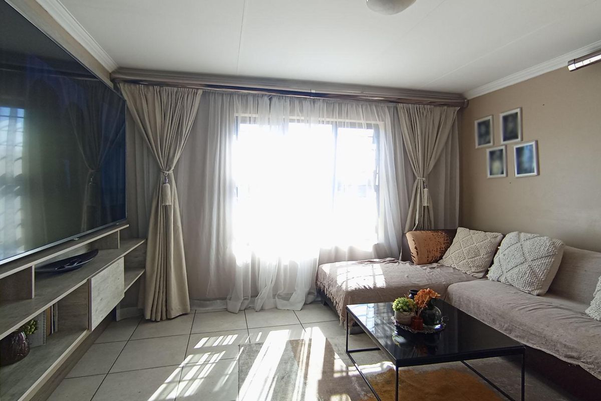 A comfortable living room featuring tiled flooring, a built-in media console, and large windows allowing for ample natural light.