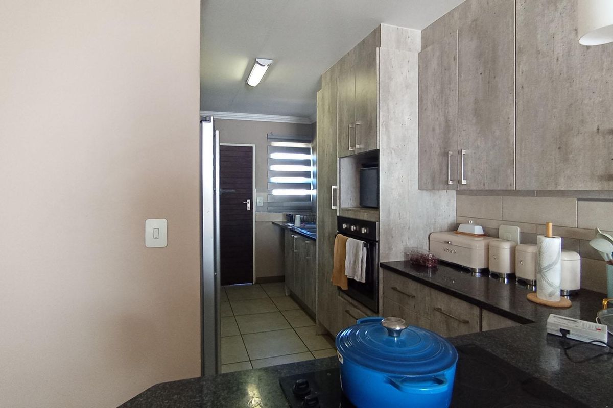 Modern kitchen featuring sleek built-in cabinetry, granite countertops, and integrated oven, leading into a functional scullery area with tiled flooring.