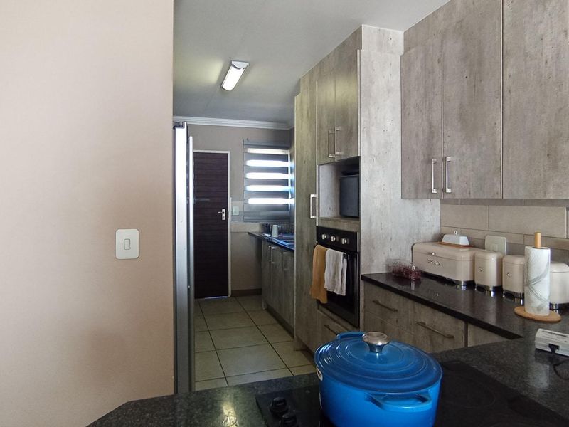 Modern kitchen featuring sleek built-in cabinetry, granite countertops, and integrated oven, leading into a functional scullery area with tiled flooring.