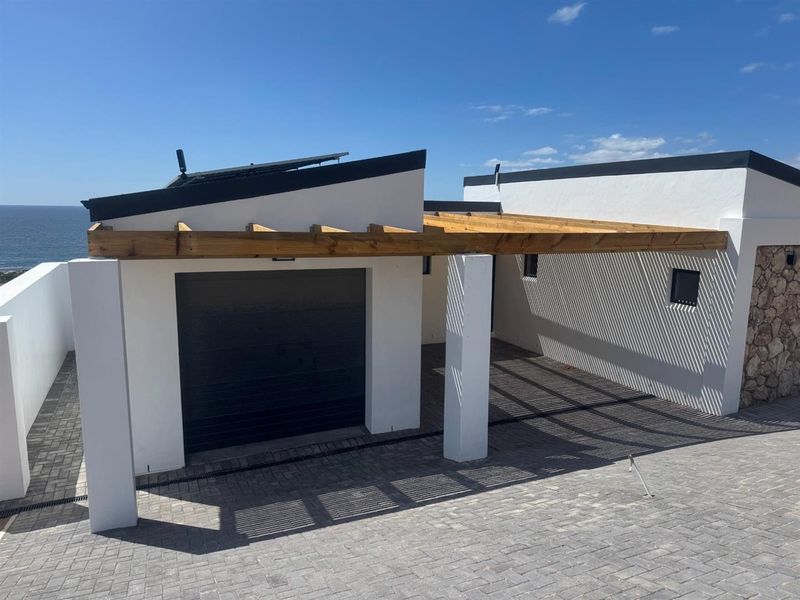 Modern exterior view of the property featuring a garage, covered carport with timber pergola, paved driveway, and solar panels on the roof.