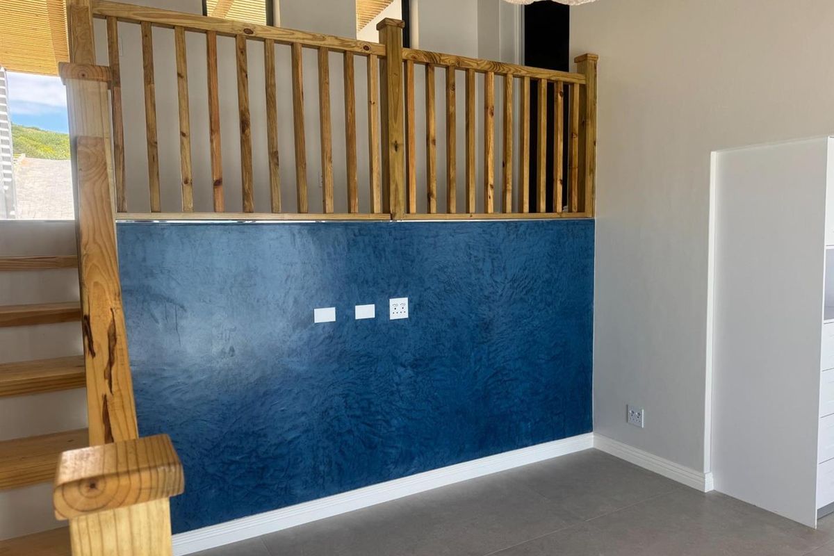 A bright living area featuring a textured blue accent wall, wooden staircase with balustrade, and neutral tiled flooring.