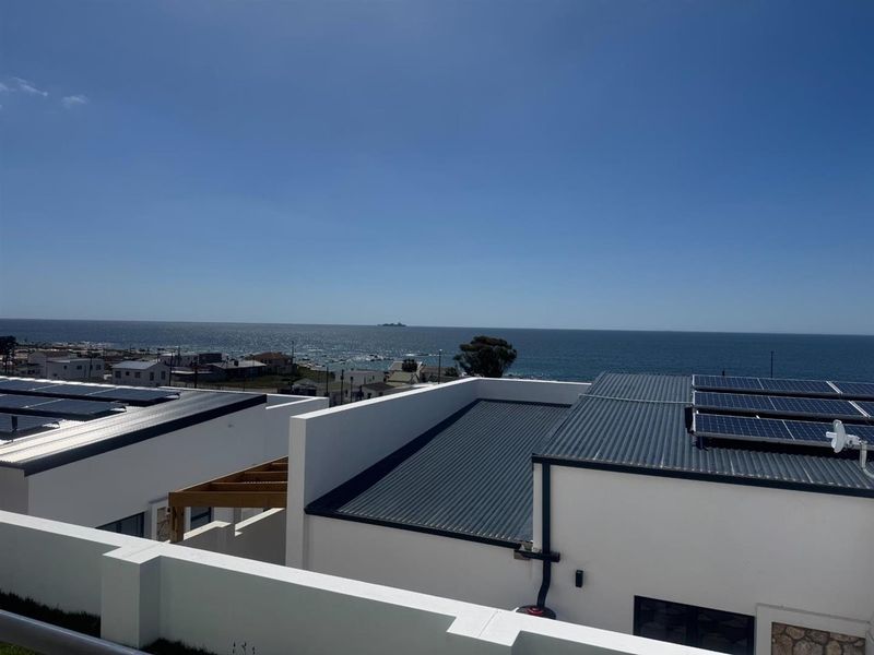 Elevated view overlooking the coastline, featuring modern flat-roofed structures equipped with integrated solar panel arrays.