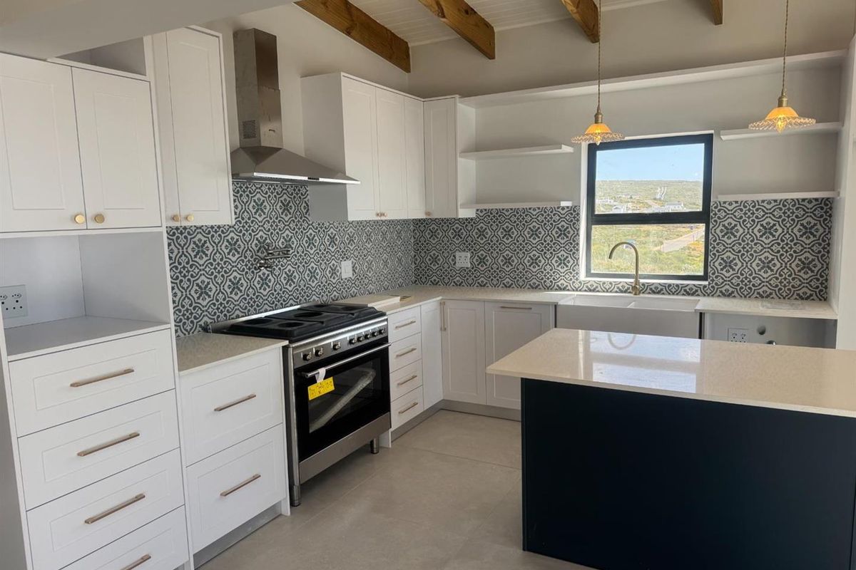 Modern kitchen featuring white cabinetry, patterned tile backsplash, stone countertops, a central island, and exposed timber ceiling beams.
