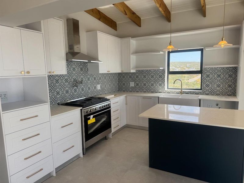 Modern kitchen featuring white cabinetry, patterned tile backsplash, stone countertops, a central island, and exposed timber ceiling beams.