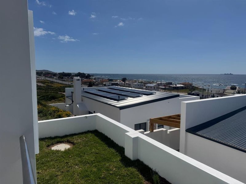 Elevated view overlooking the property roof with installed solar panels, featuring a coastal landscape and ocean horizon.