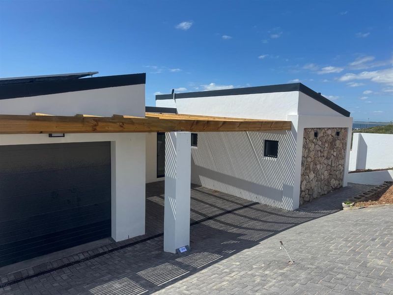 Modern exterior front view featuring a paved driveway, covered carport with timber pergola, stone cladding accents, and a sleek contemporary roofline.