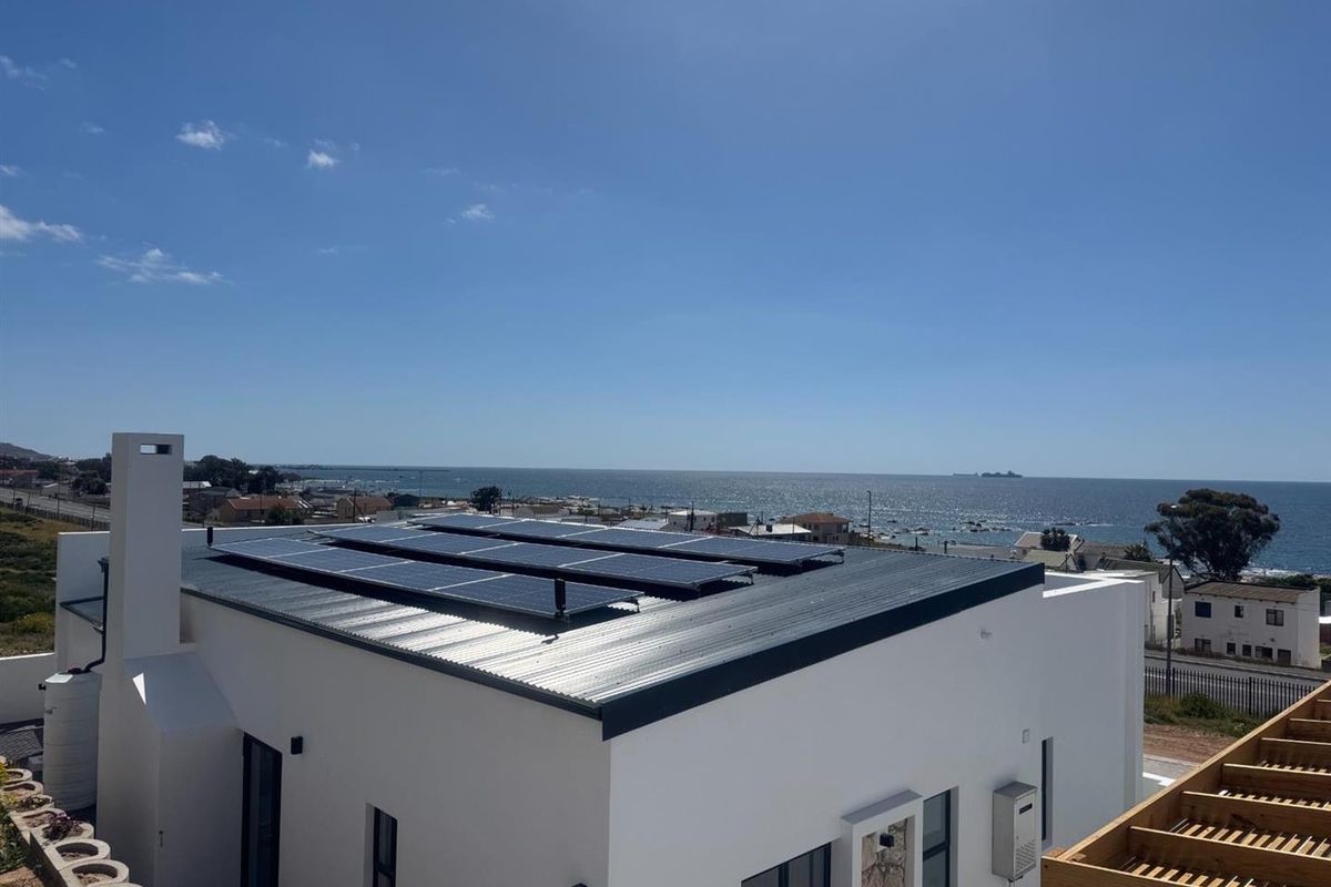 Elevated view of the property roof featuring a modern solar panel installation, overlooking the coastal landscape and ocean.