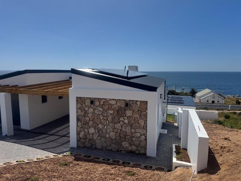 Modern coastal home exterior featuring stone cladding, solar panels, a timber pergola, and paved driveway with scenic ocean views.