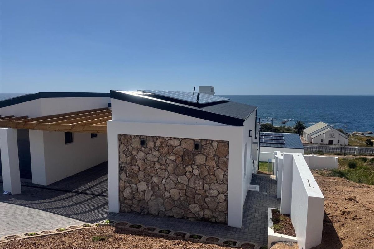 Modern coastal home exterior featuring stone cladding, solar panels, a timber pergola, and paved driveway with scenic ocean views.