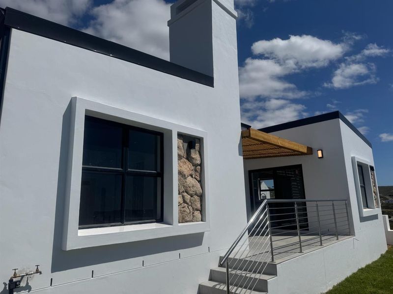 A modern exterior view of the house featuring a clean white facade, stone accent detailing, a timber pergola, and a stainless steel staircase railing.