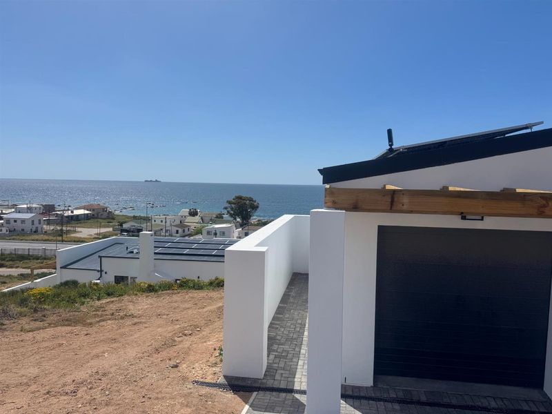 Modern exterior view featuring a garage with a paved walkway, solar panels on the roof, and a scenic coastal outlook.