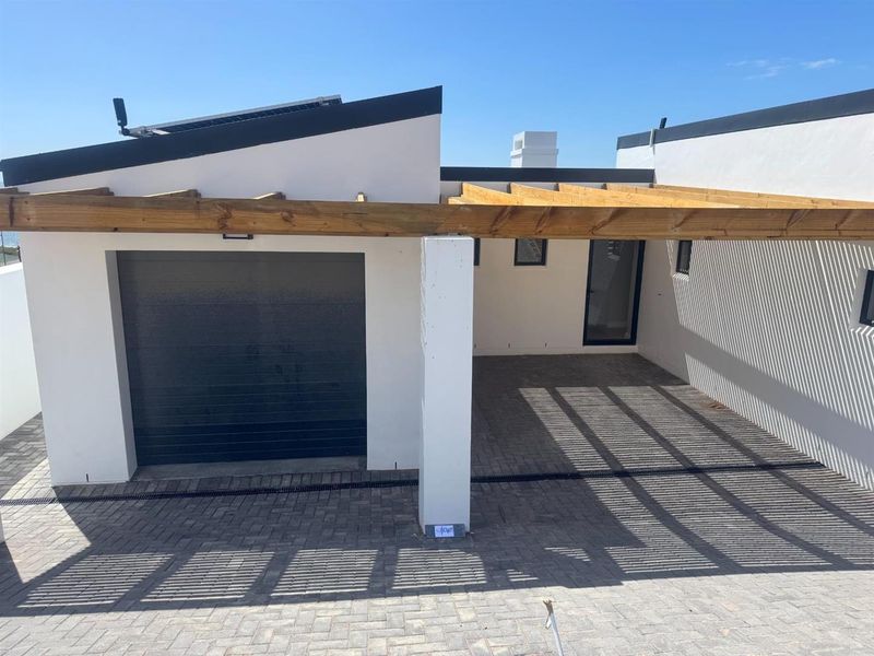 Modern exterior view featuring a single garage, paved driveway, and a timber pergola structure providing shaded parking space.