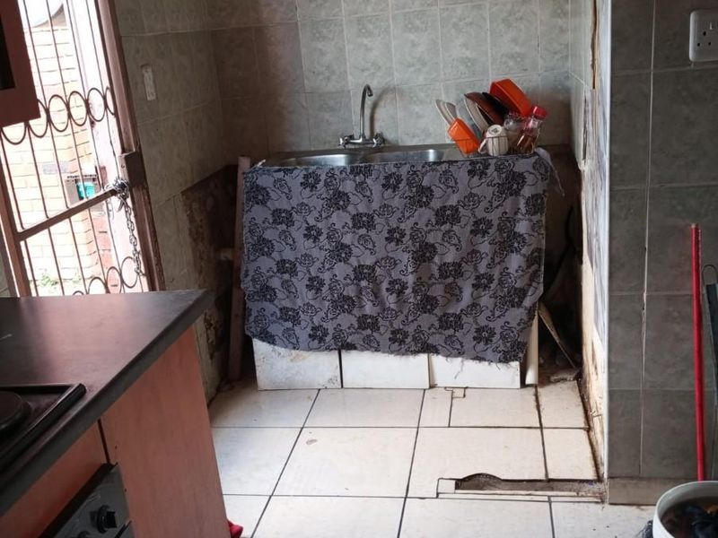 A dated kitchen area featuring a stainless steel sink, built-in oven, and tiled finishes, currently requiring significant maintenance and renovation to restore functionality.