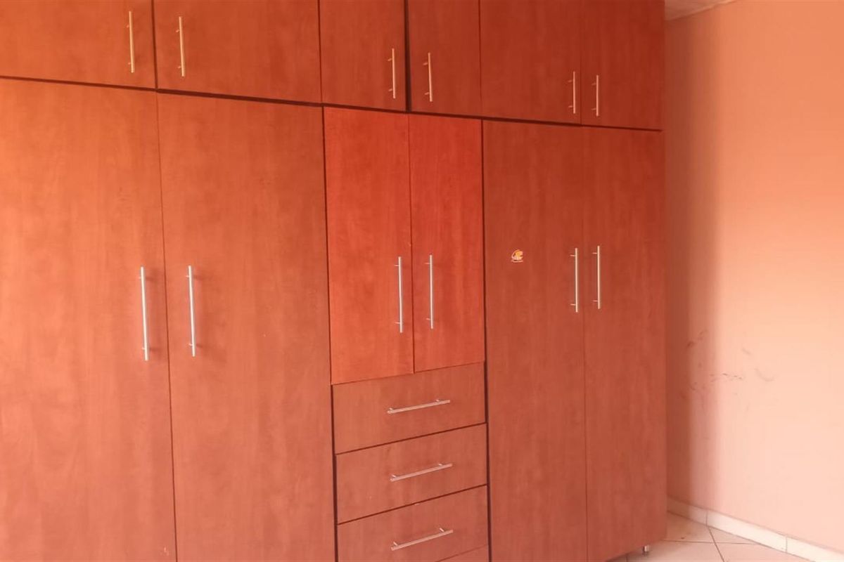 A bedroom featuring extensive built-in wooden cabinetry with integrated drawers and overhead storage, finished with tiled flooring.