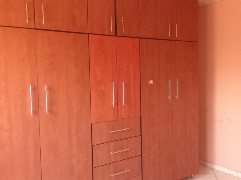 A bedroom featuring extensive built-in wooden cabinetry with integrated drawers and overhead storage, finished with tiled flooring.