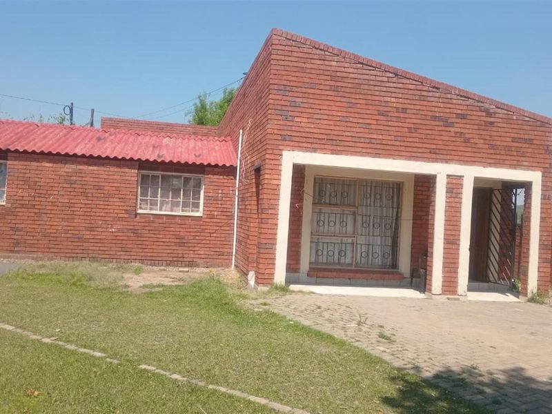 Front view of a face brick house featuring a covered entrance, security bars on windows, and a paved driveway area.