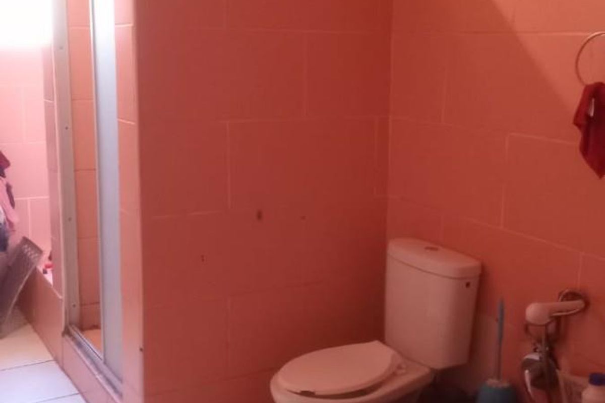 A functional bathroom featuring a shower enclosure, toilet, and full-height wall tiling in a dated peach finish.