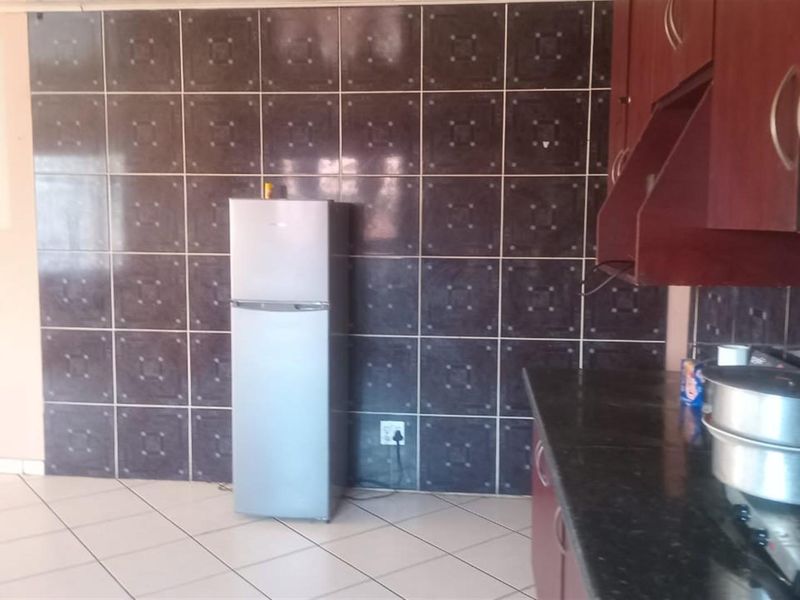 A kitchen area featuring dark tiled splashbacks, built-in cabinetry, and tiled flooring, offering a functional space with potential for modern updates.