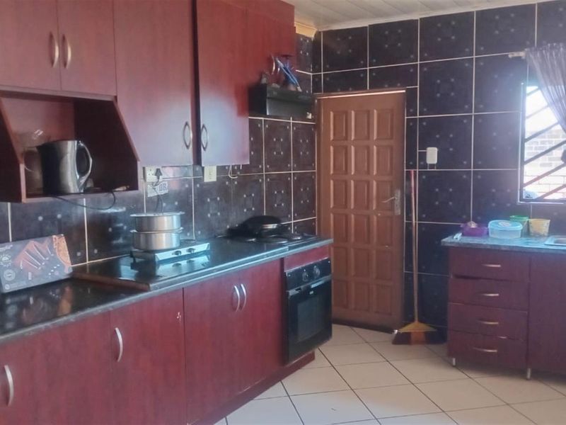 A functional kitchen featuring dark wood-finish cabinetry, tiled backsplash, built-in oven with hob, and a double sink with tiled flooring.