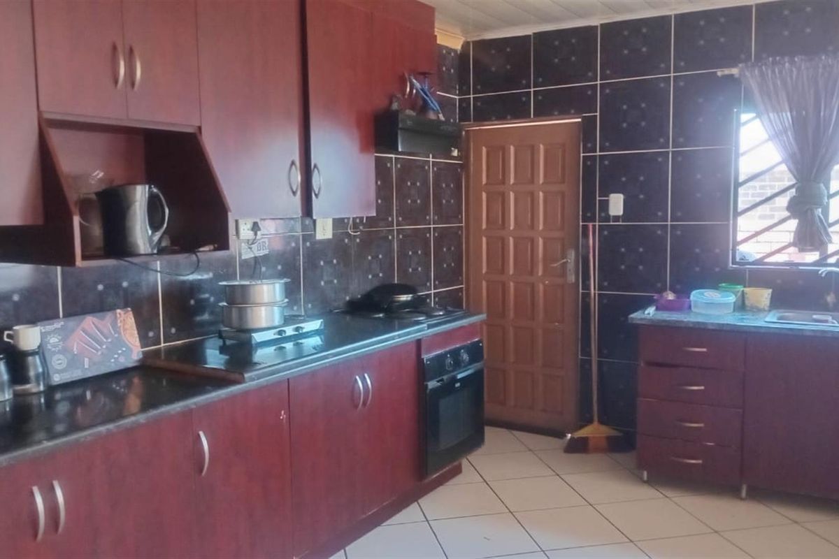 A functional kitchen featuring dark wood-finish cabinetry, tiled backsplash, built-in oven with hob, and a double sink with tiled flooring.