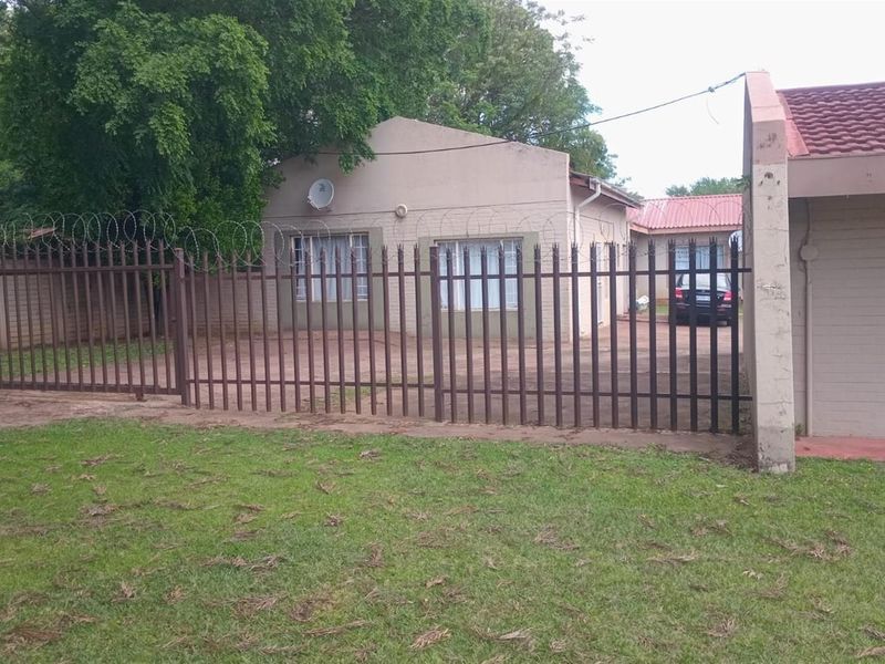 Front view of a commercial property featuring a paved driveway, secure steel palisade fencing with razor wire, and a tiled roof structure.