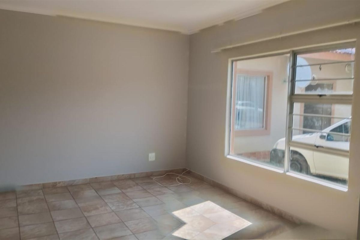 A bright, empty living area featuring neutral wall tones, tiled flooring, and large windows with security bars, offering a clean canvas for customization.