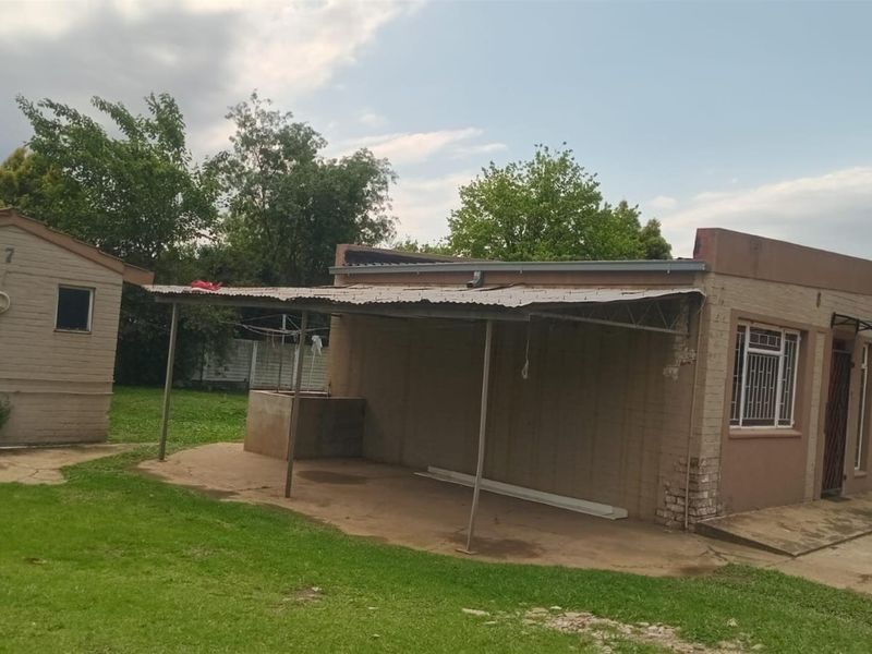 Rear view of the commercial property featuring a covered patio area, brick exterior walls, and metal roofing with visible signs of wear.