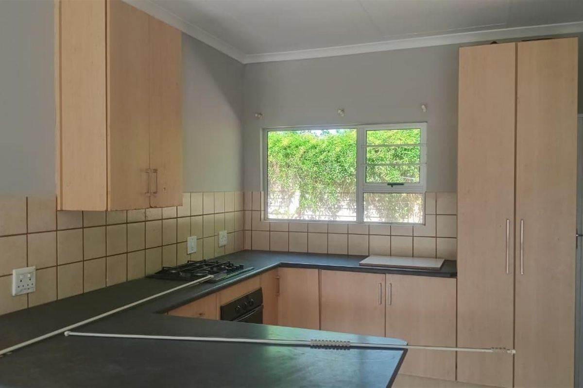 A functional kitchen featuring light wood-finish cabinetry, dark laminate countertops, a built-in gas hob, and an oven, with a window overlooking the garden.