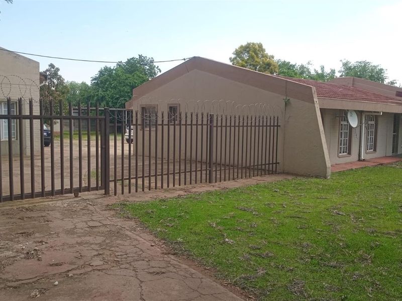 Front exterior view of a commercial property featuring a paved driveway, lawn, and secure metal fencing with razor wire.
