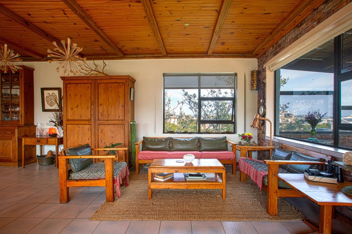 A rustic living room featuring a timber-paneled ceiling, exposed brick wall accents, and large windows providing natural light and exterior views.