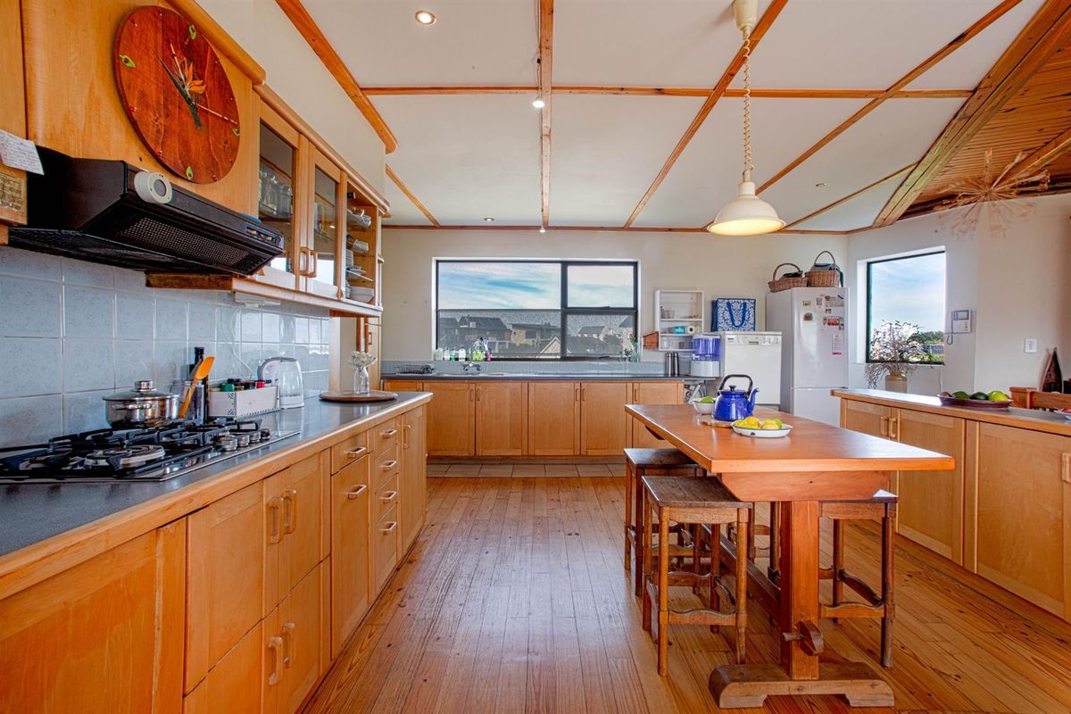 Spacious kitchen featuring timber cabinetry, gas hob, extractor fan, and a central island, with large windows providing natural light and views.