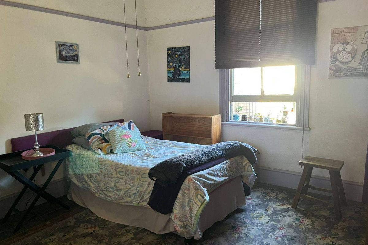 A bedroom featuring a window with fitted blinds, high ceilings with picture rails, and patterned carpet flooring.