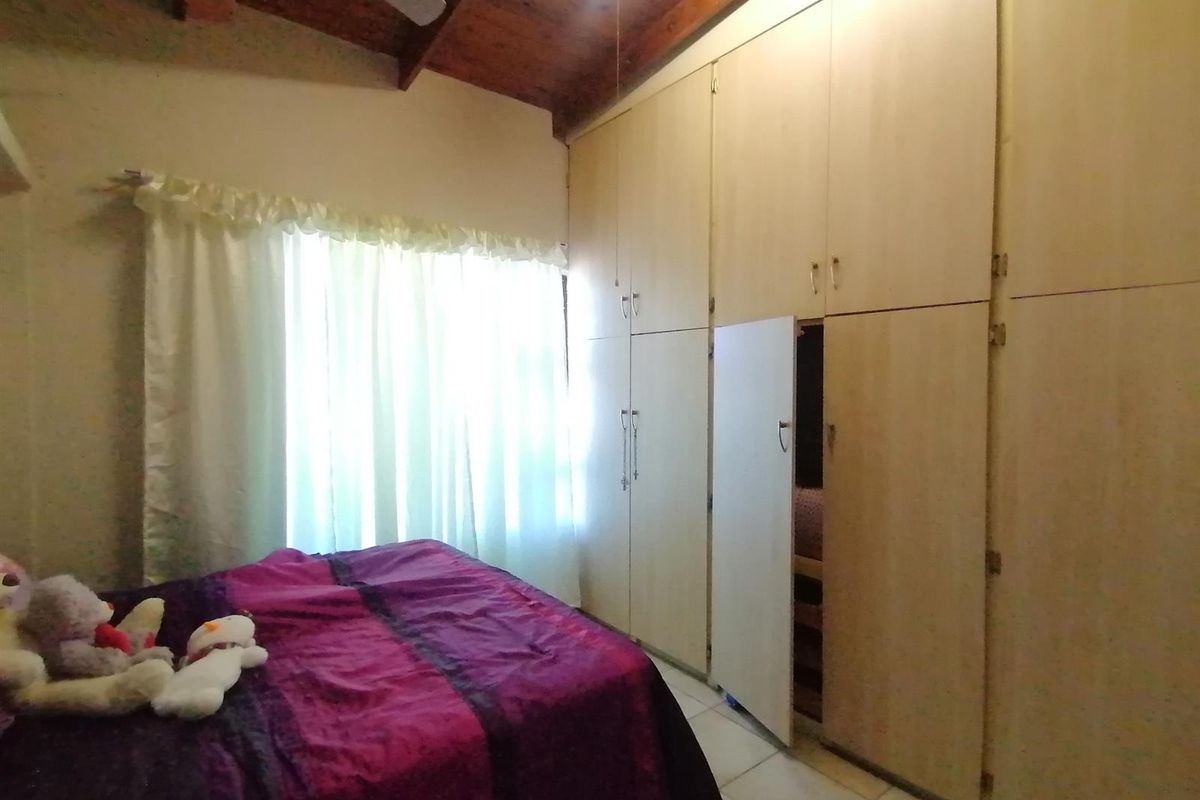 Bedroom featuring extensive built-in floor-to-ceiling cupboards, tiled flooring, and an exposed timber vaulted ceiling with a fitted fan.