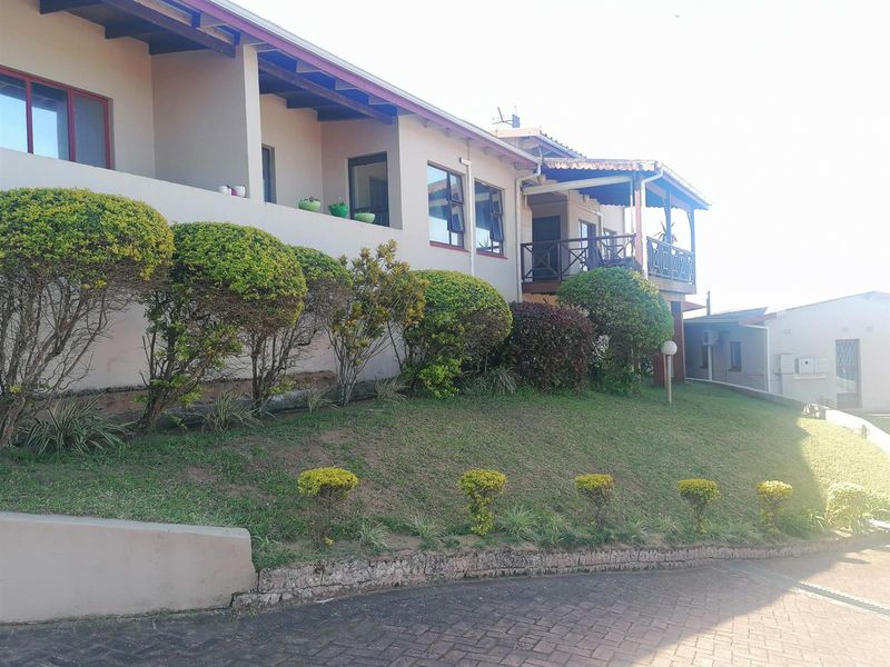 Rear exterior view of the townhouse featuring a raised balcony with timber railings, landscaped garden beds, and a paved driveway area.