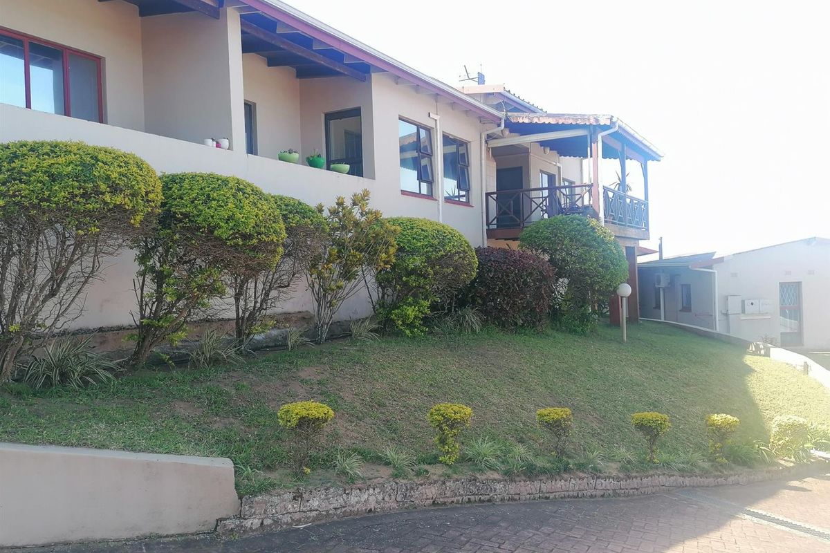 Rear exterior view of the townhouse featuring a raised balcony with timber railings, landscaped garden beds, and a paved driveway area.
