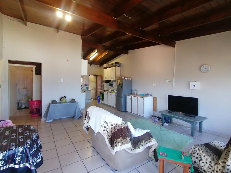 Open-plan living and kitchen area featuring high exposed timber beam ceilings and tiled flooring, offering a functional layout with potential for modern updates.
