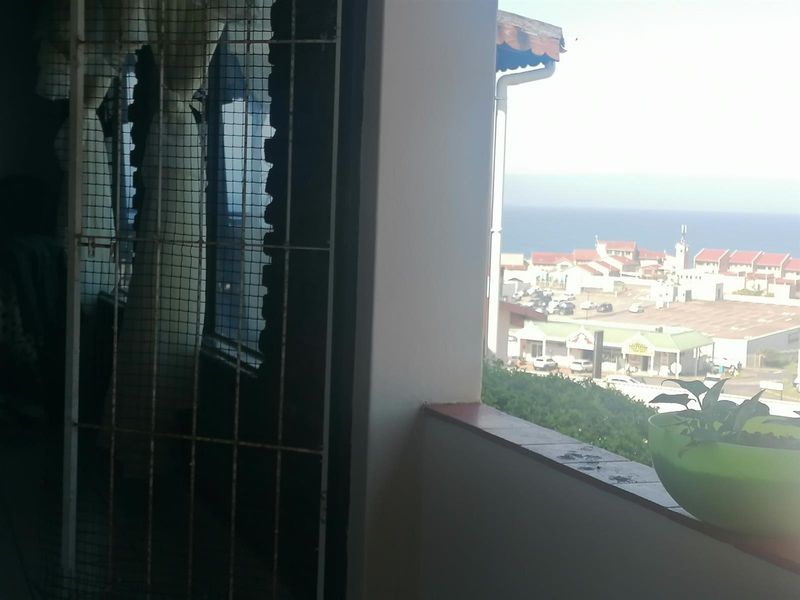 A balcony area featuring a security gate and a tiled ledge, offering an elevated view of the surrounding neighborhood and distant coastline.