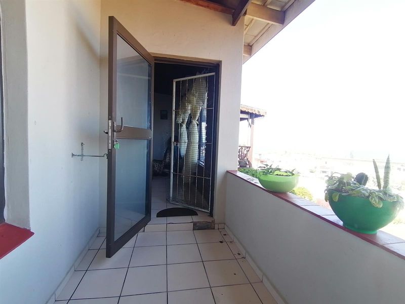 A covered balcony area featuring tiled flooring, a security gate, and an aluminium door frame, offering an outdoor space with potential for enhancement.
