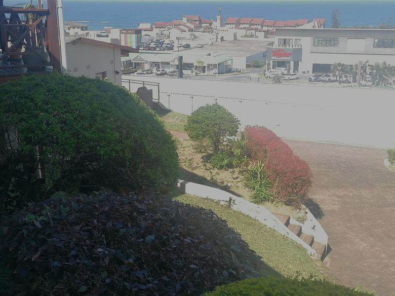 Elevated view overlooking a landscaped garden area with a retaining wall, paved pathway, and surrounding neighbourhood infrastructure.