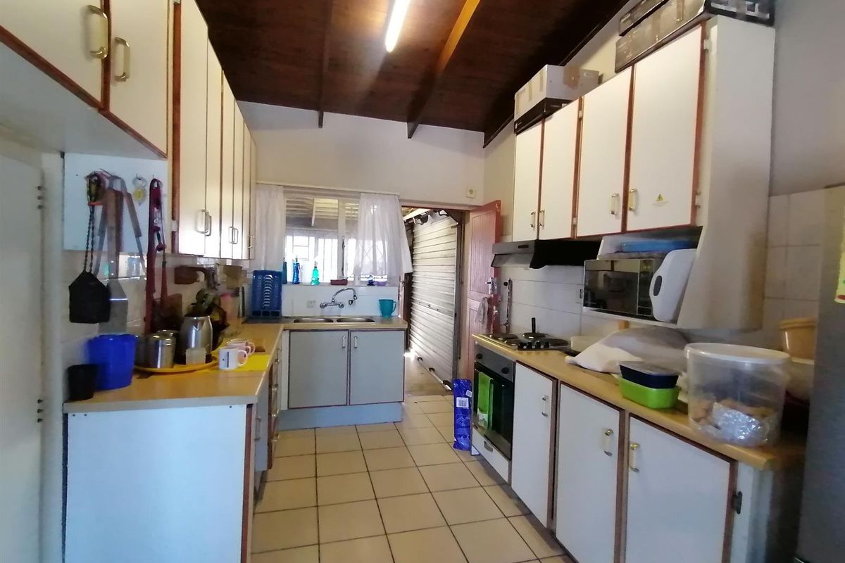 A dated galley-style kitchen featuring built-in cabinetry, laminate countertops, a built-in oven, and exposed timber ceiling beams.